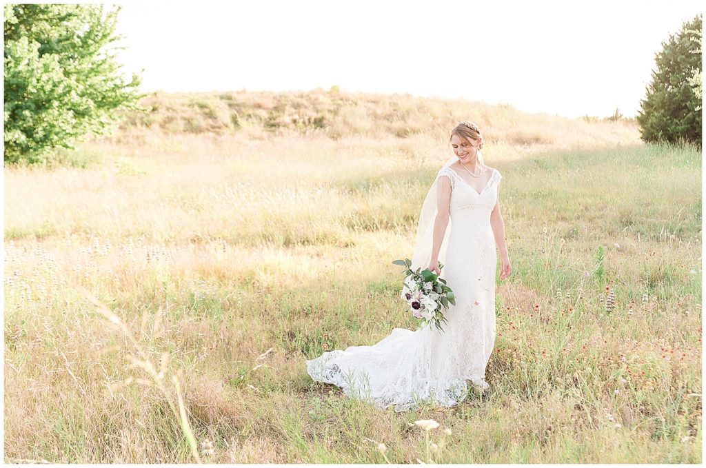 bride walking in field at arbor hills in lace gown with peony and rose bouquet