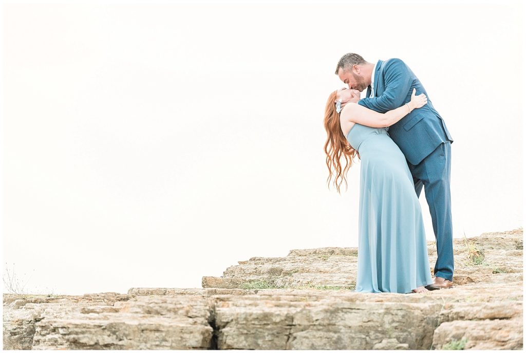 engaged couple dip kiss on cliff at rockledge park in grapevine texas blue dress