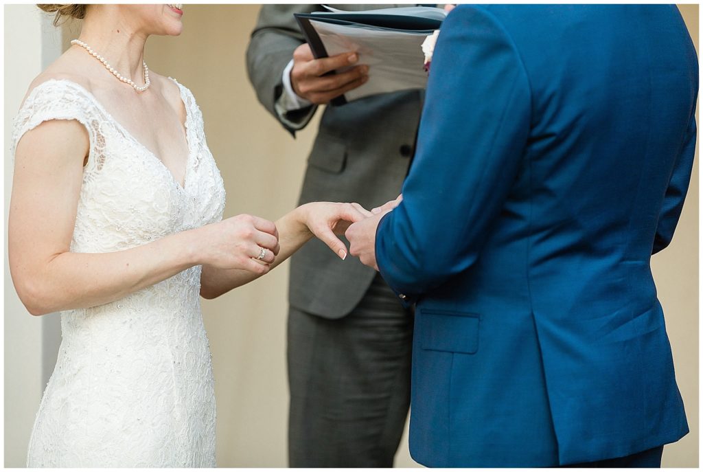 groom in navy suit placing ring on bride's finger