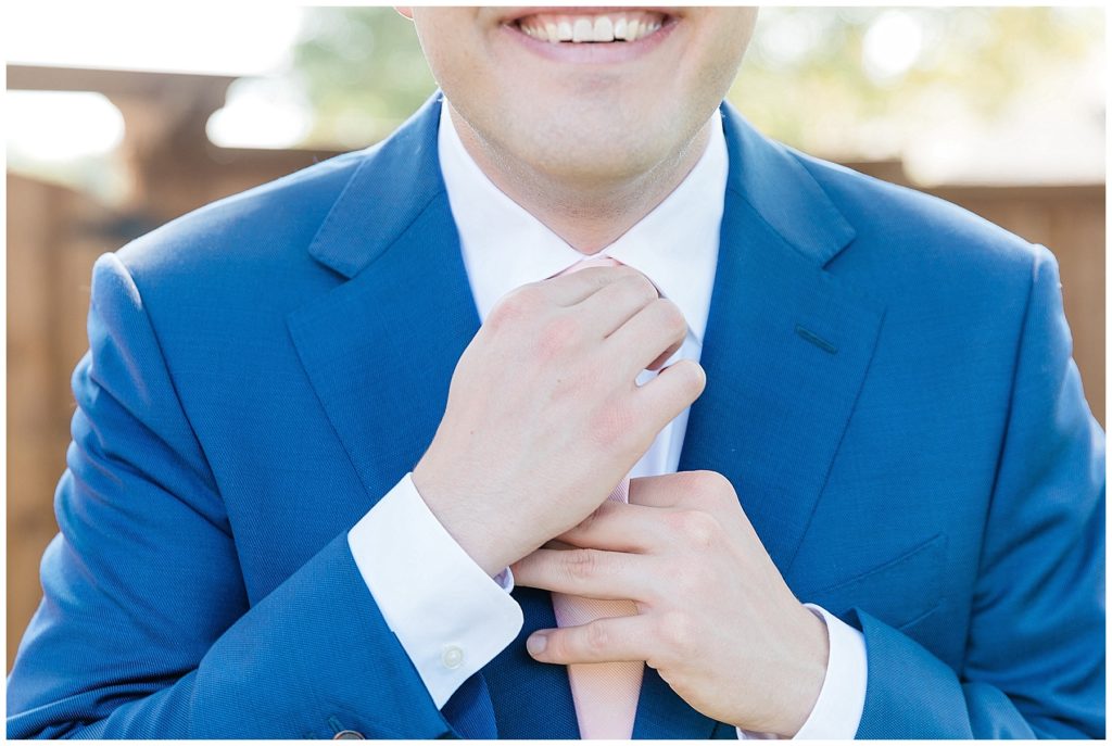 groom in navy suit adjusting pink tie