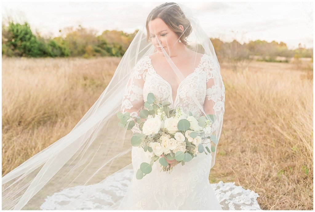 bride under cathedral length veil with white rose bouquet in field in texas