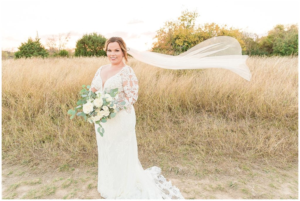 bride in lace gown with v neckline and cathedral length veil blowing in the wind