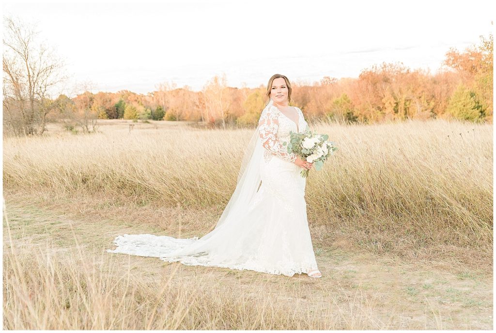 bride in lace gown and cathedral length veil in field at clear creek natural heritage center in denton texas