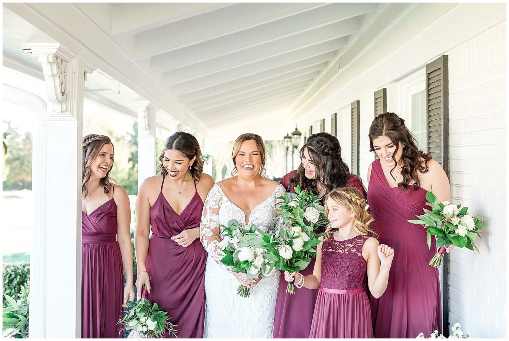 bridesmaids in burgundy dresses laughing with bride in white lace dress