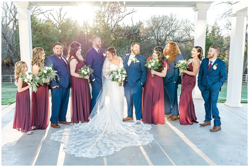 wedding party laughing under white pergolas bridesmaids in burgundy dresses groomsmen in navy suits
