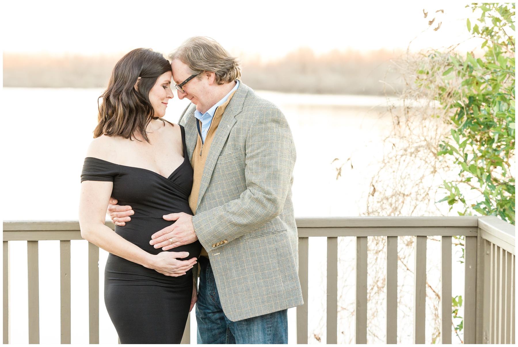 husband and wife hug on pier along Red River in Shreveport LA during maternity photos 