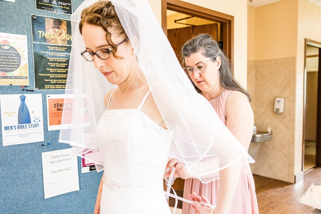 bridesmaid helps bride with wedding gown 