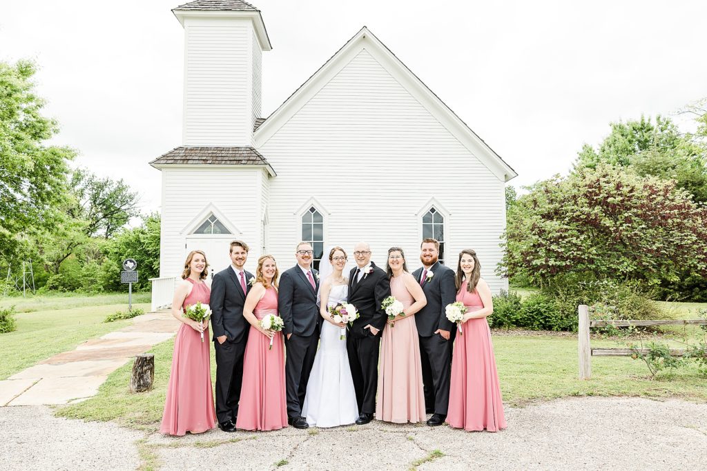 newlyweds pose with wedding party outside white church