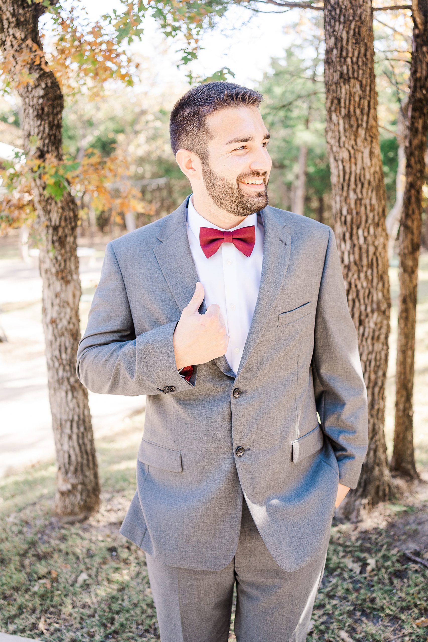 groom holds lapel of grey suit with red bowtie
