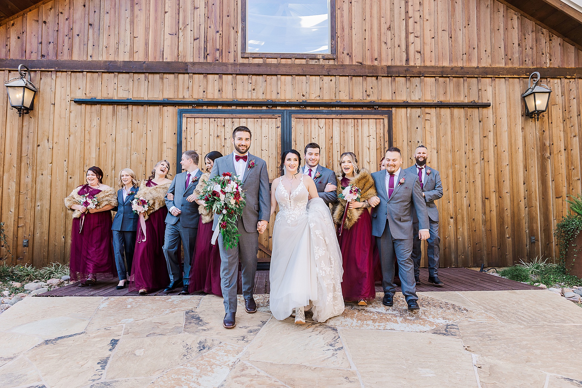 bride and groom hold hands walking in front of wooden barn at Whispering Oaks with wedding party