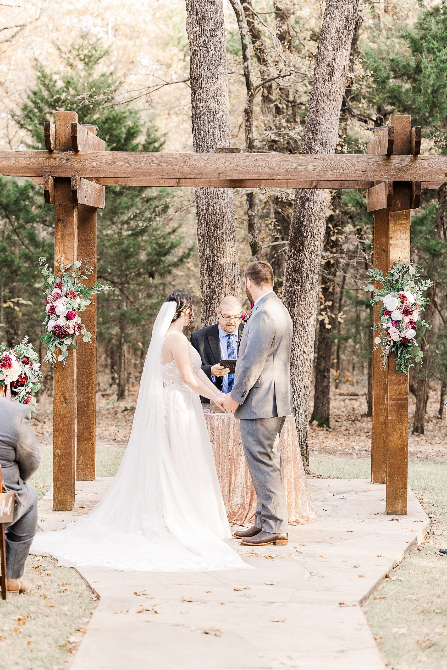couple holds hands by wooden arbor for outdoor wedding ceremony in North Texas