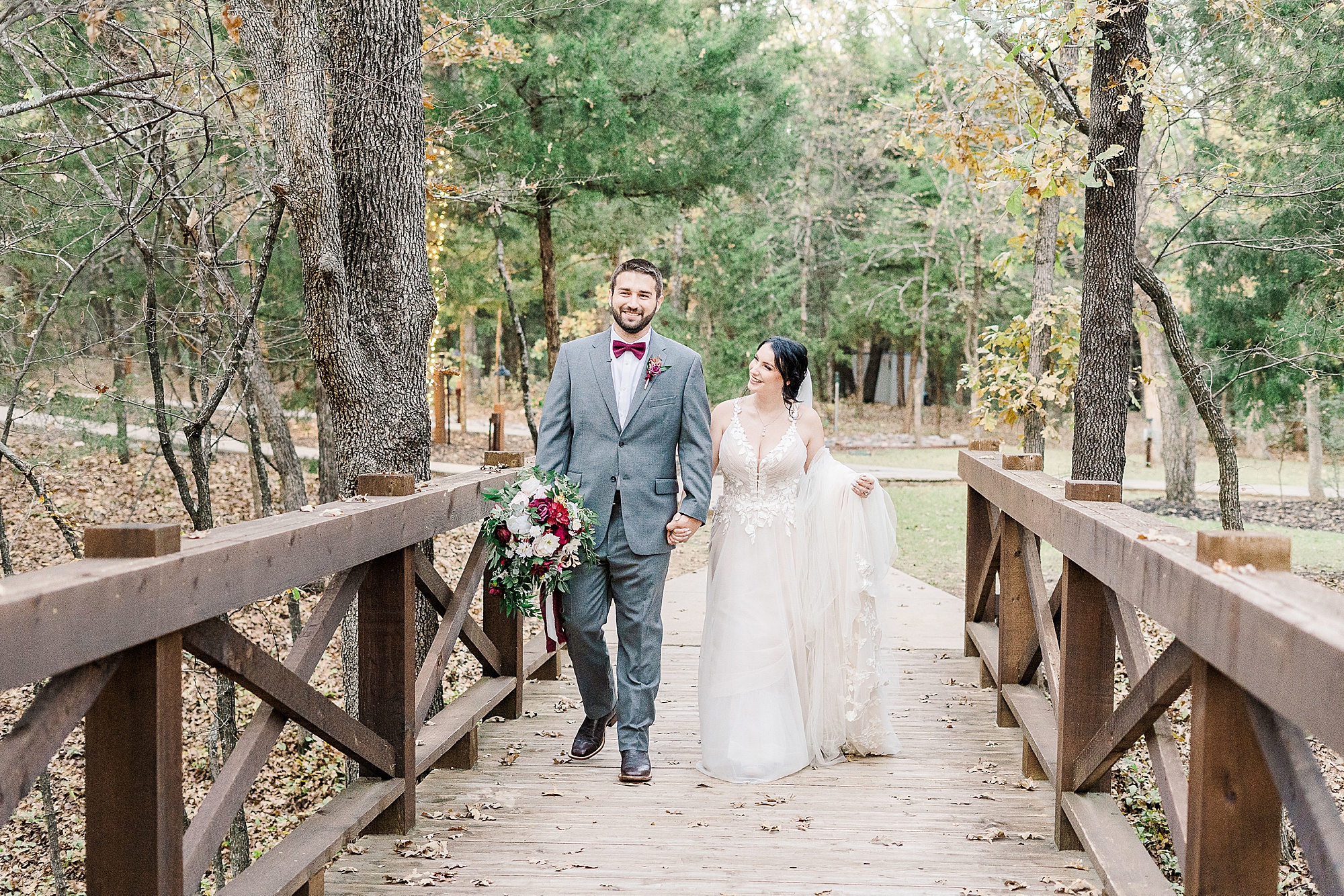 newlyweds walk over wooden bridge at Whispering Oaks
