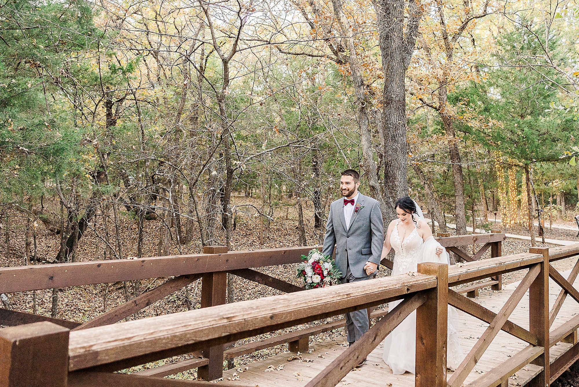 bride and groom walk over wooden bridge at Whispering Oaks