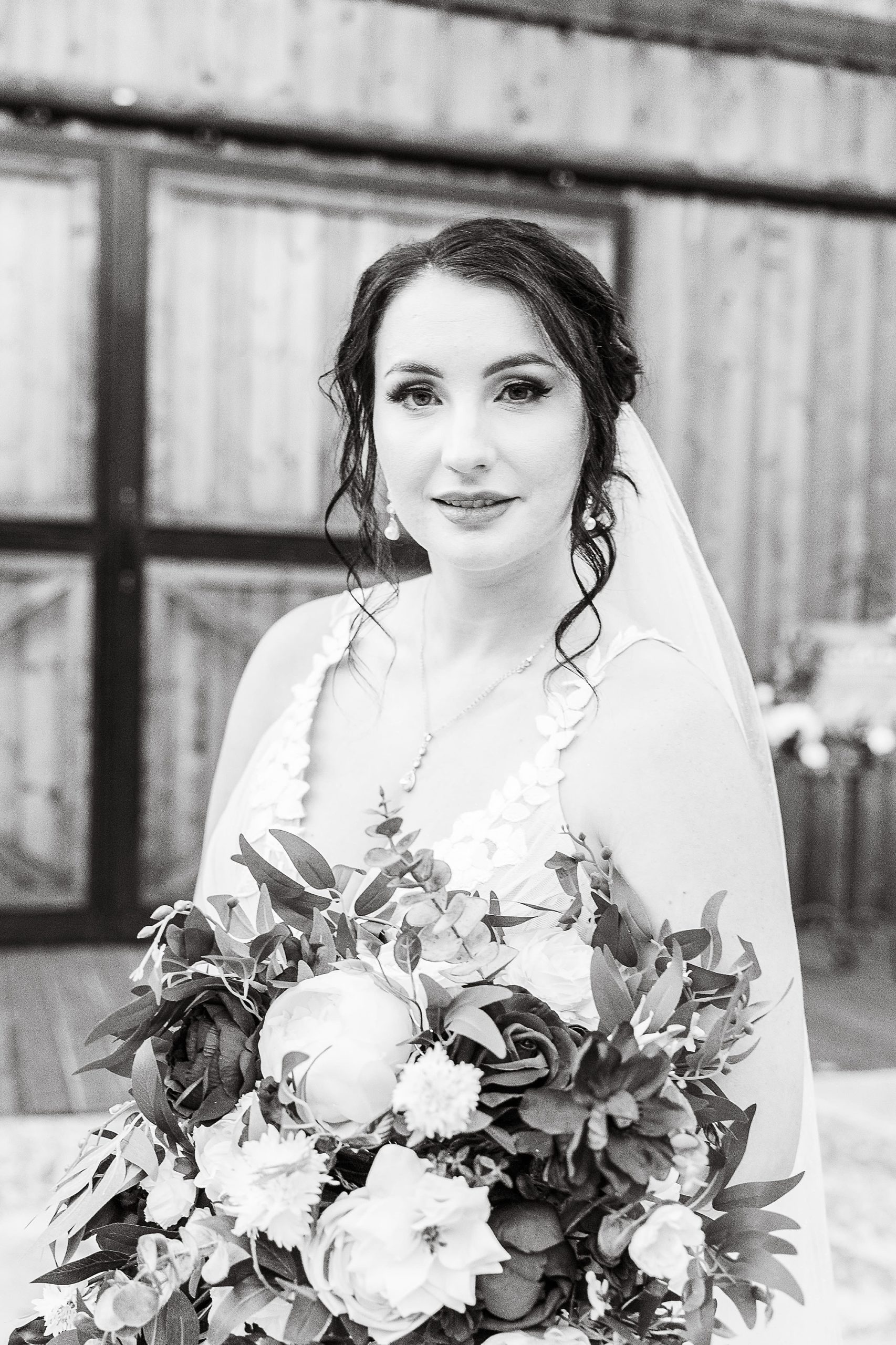 bride stands holding bouquet with veil around shoulder