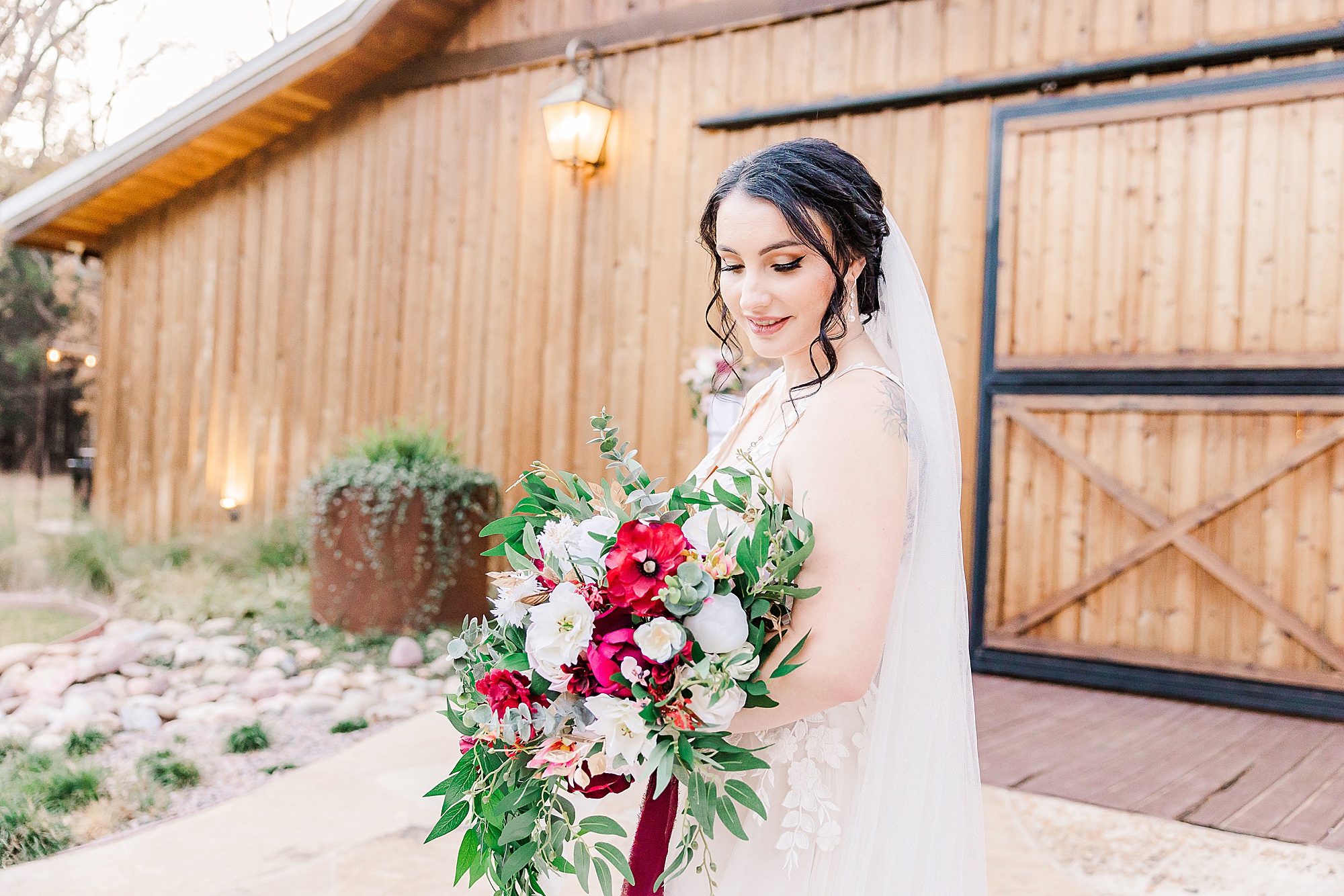 bride looks down at bouquet with red and white flowers