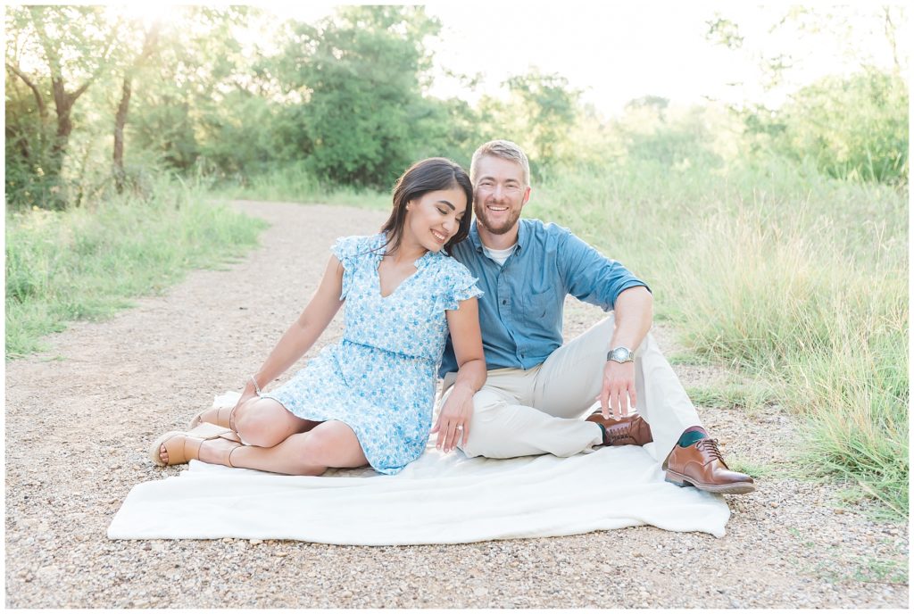 engaged couple at clear creek natural heritage center in denton texas sitting on trail in grassy field engagement session