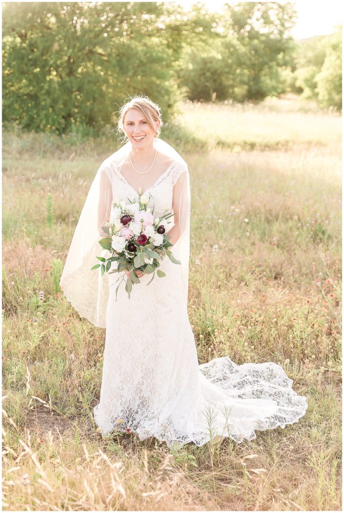 bride walking in field at arbor hills in lace gown with peony and rose bouquet