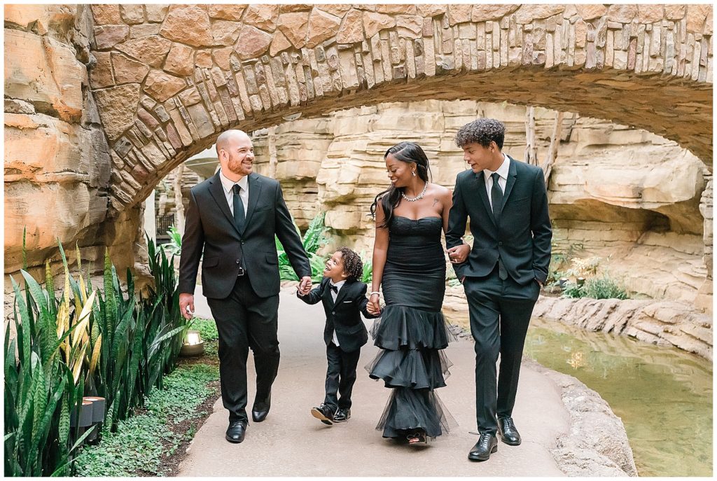 family in black couture and tuxedos walking on riverwalk