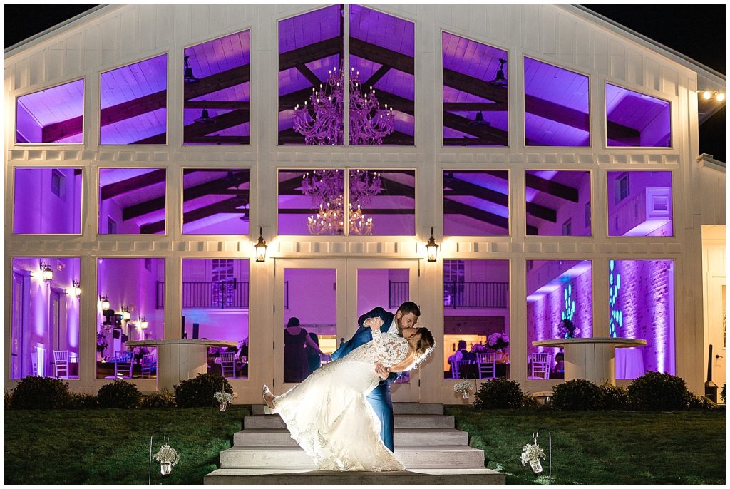 bride and groom dip kiss in front of wall of windows with purple lighting