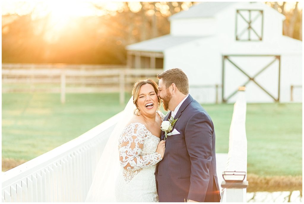 bride and groom at golden hour on bridge in front of white barn
