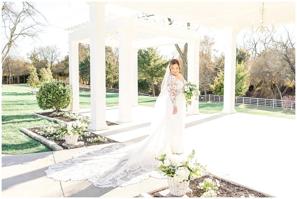 bride in lace gown with v neckline with cathedral length veil under white pergola