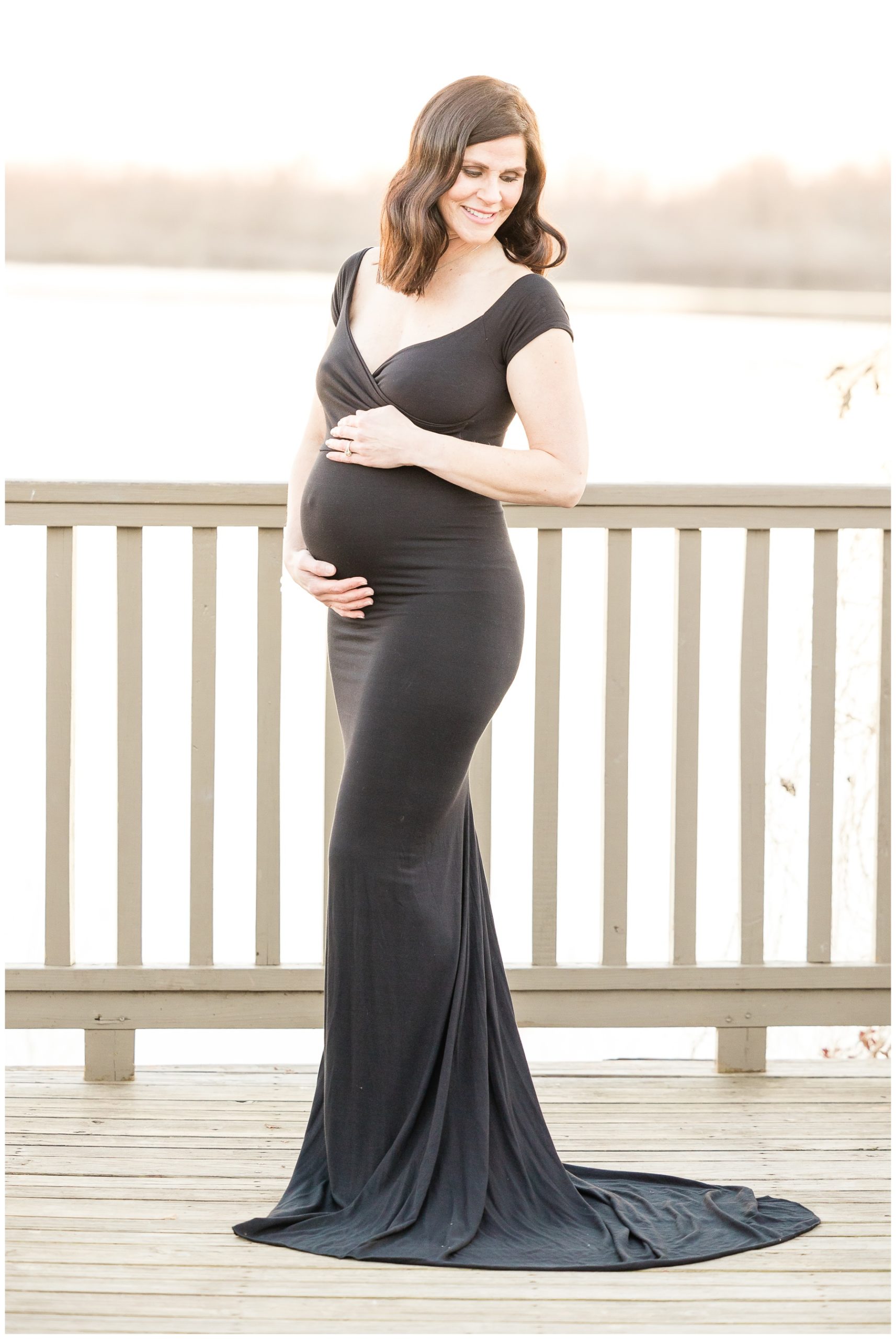 mom in black dress hugs belly during Red River National Heritage Center maternity portraits