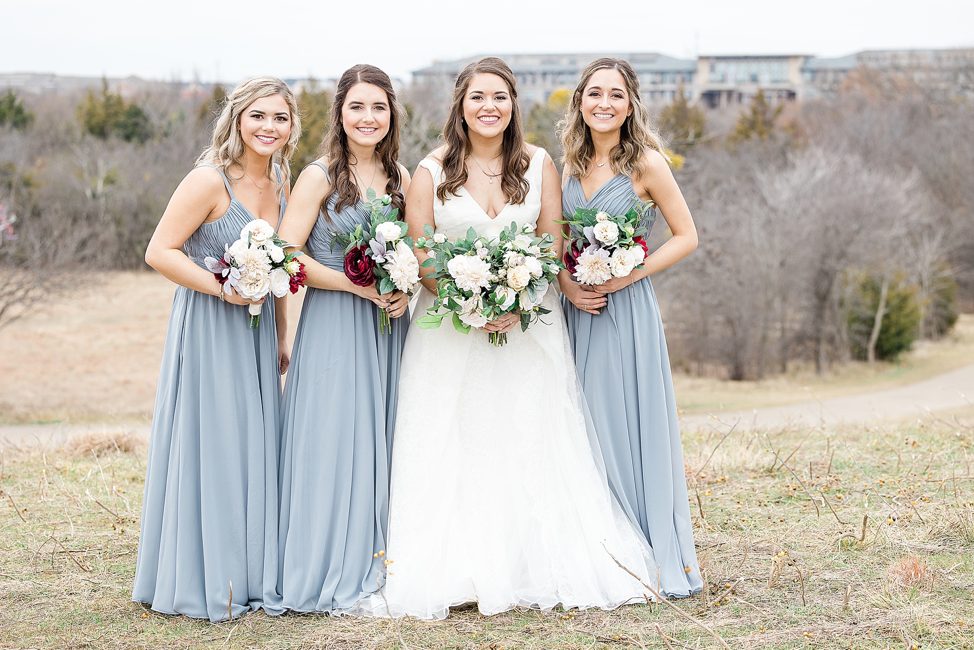 bride and bridesmaids in light blue gowns pose on hill at Arbor Hills Nature Preserve