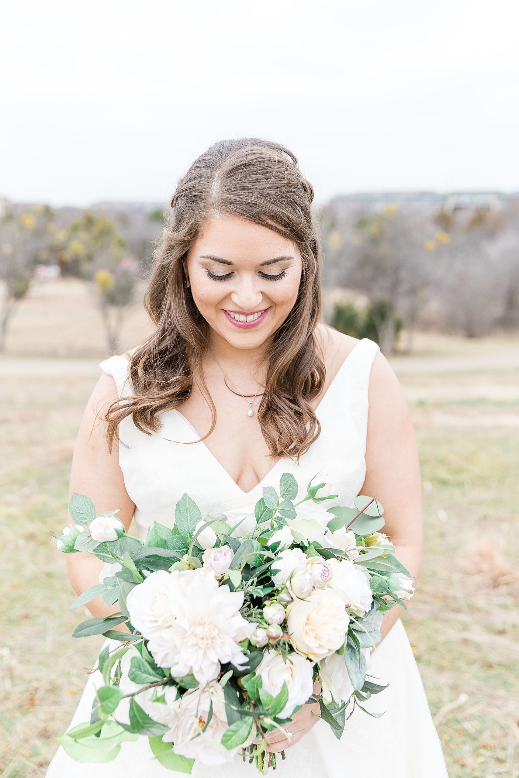 bride looks down at bouquet of light flowers for winter wedding