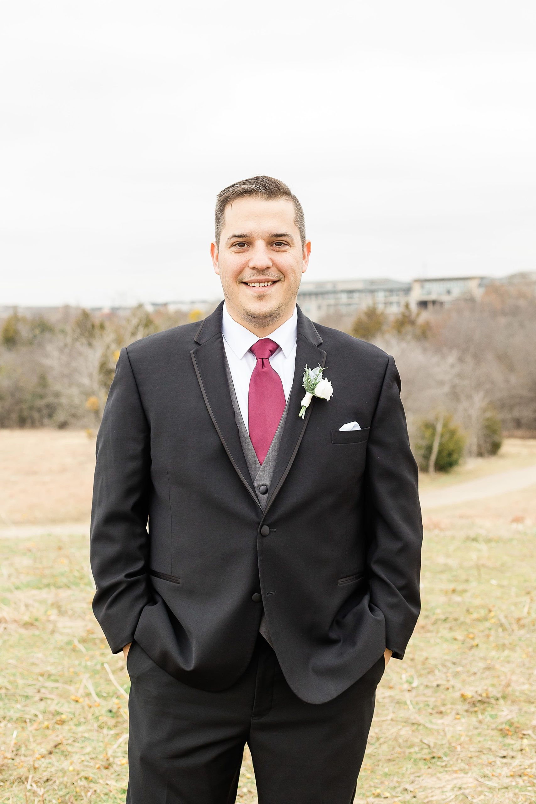groom in grey suit and red tie poses during winter wedding portraits 