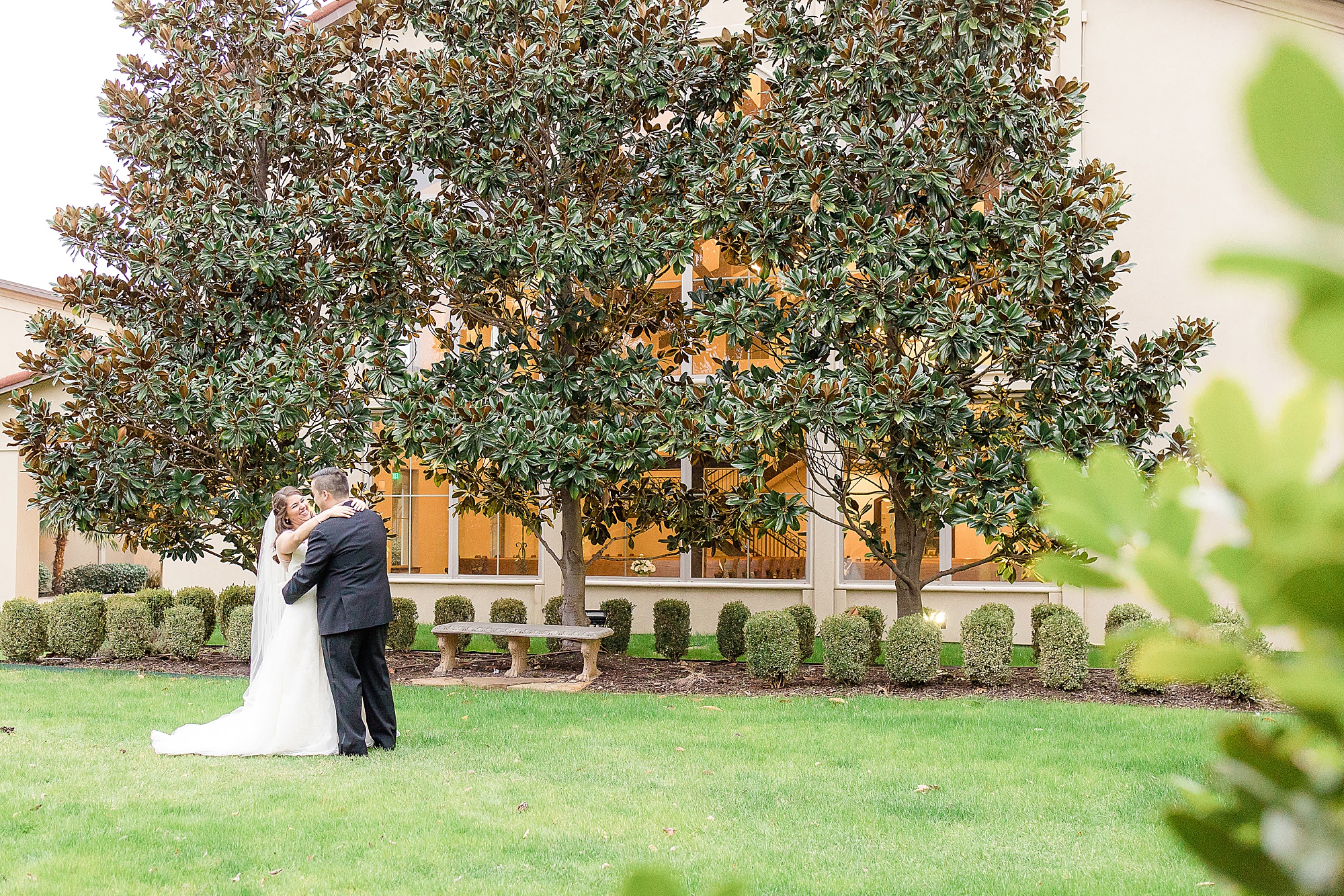 bride and groom hug by tree in courtyard of the Chapel at Ana Villa