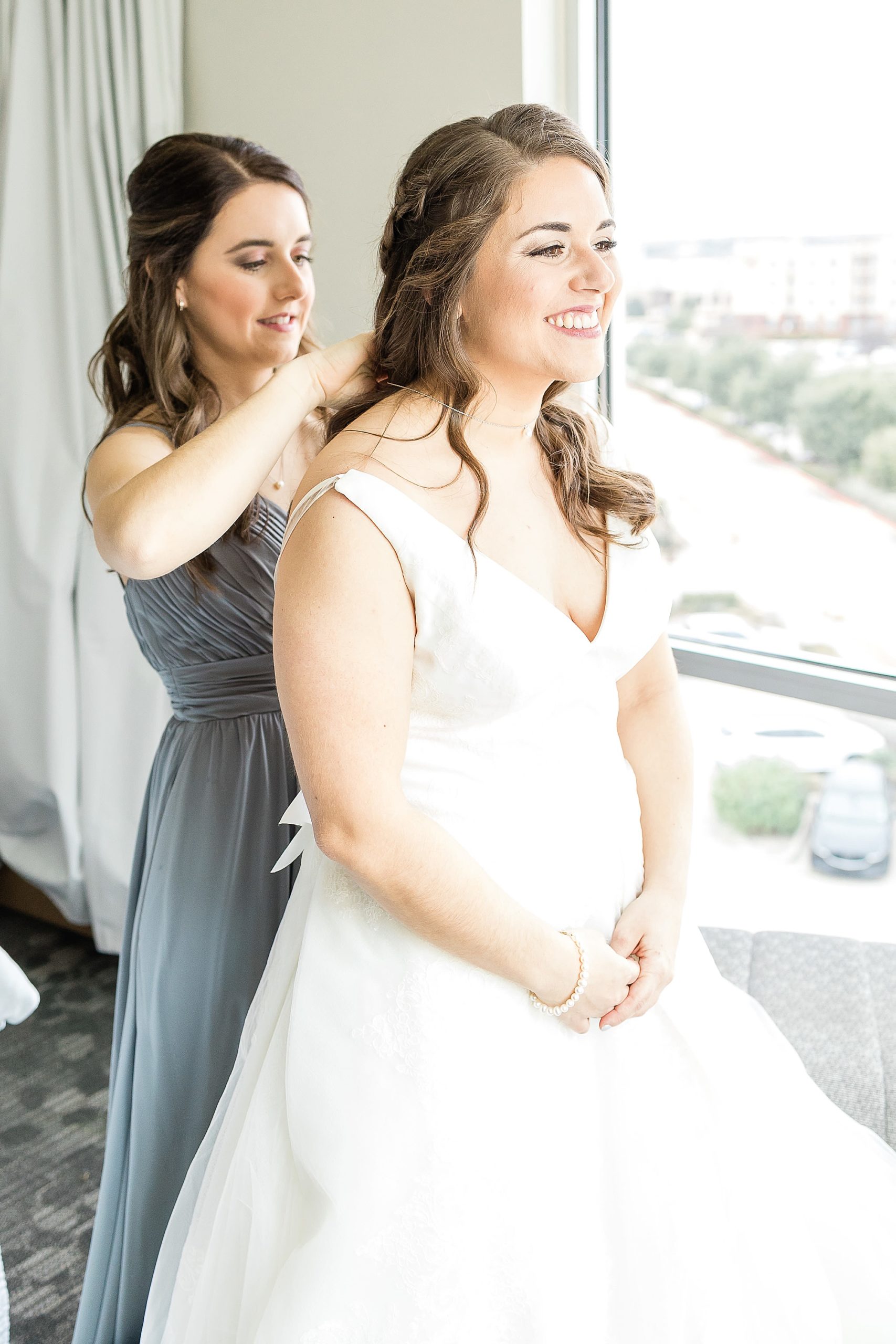 bridesmaid helps bride with jewelry on wedding morning 