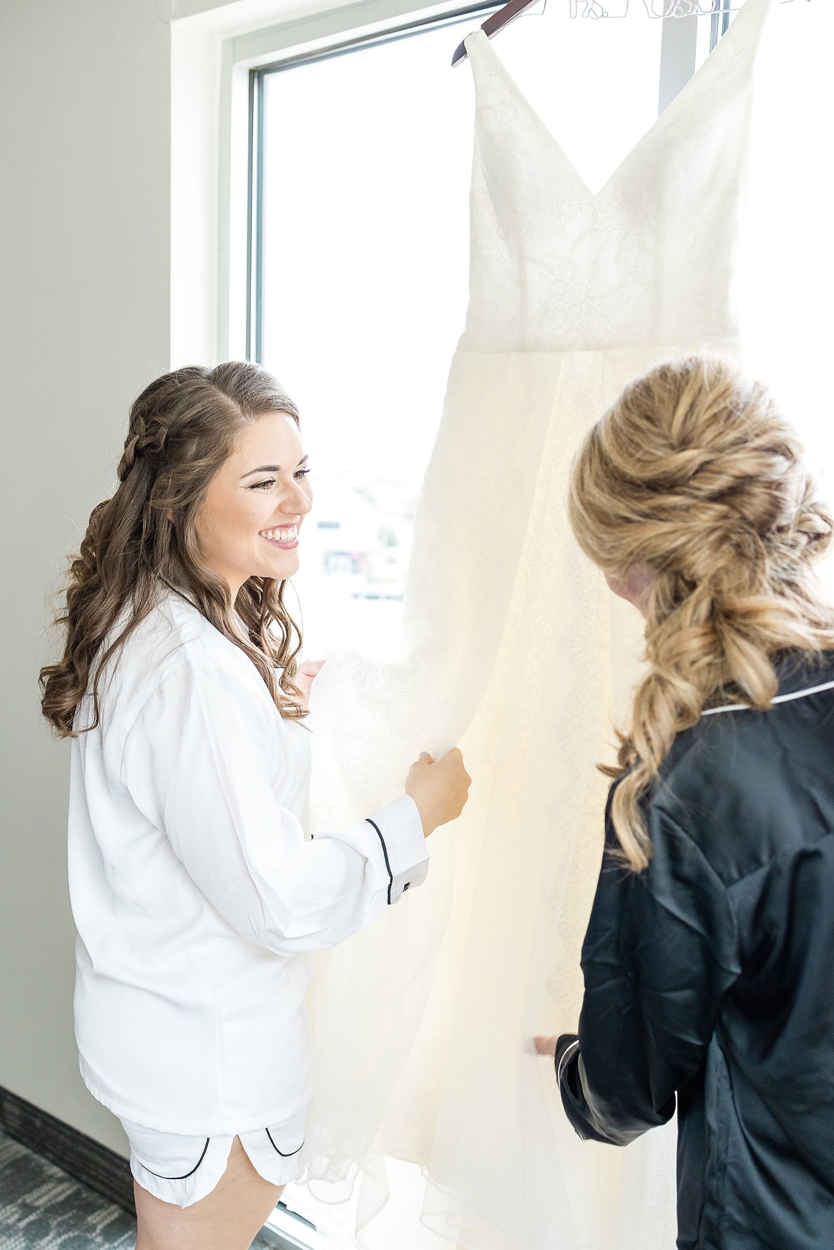 bride smiles at bridesmaid looking at wedding gown