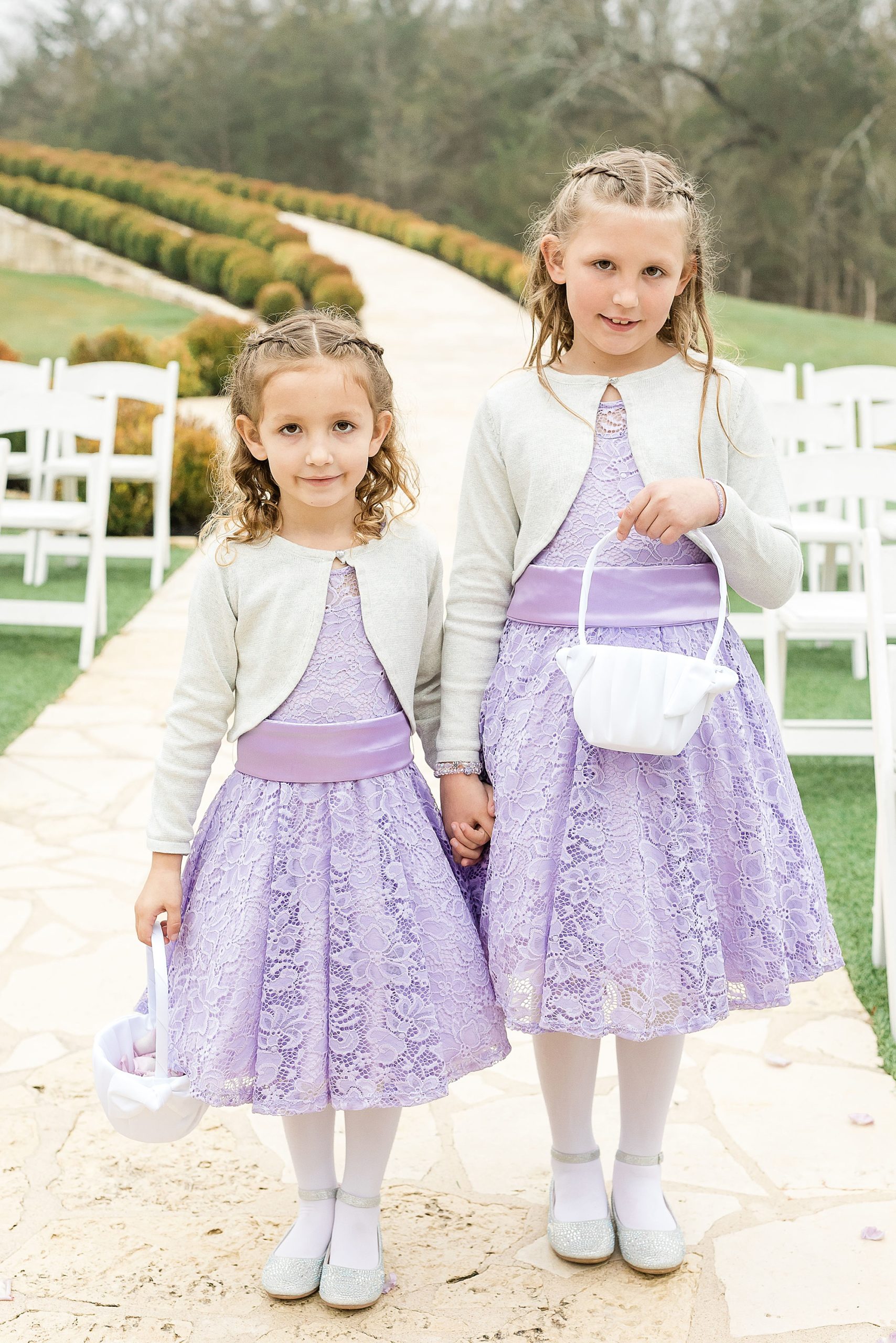 flower girls in purple dresses walk down aisle at outdoor wedding ceremony in Anna Texas