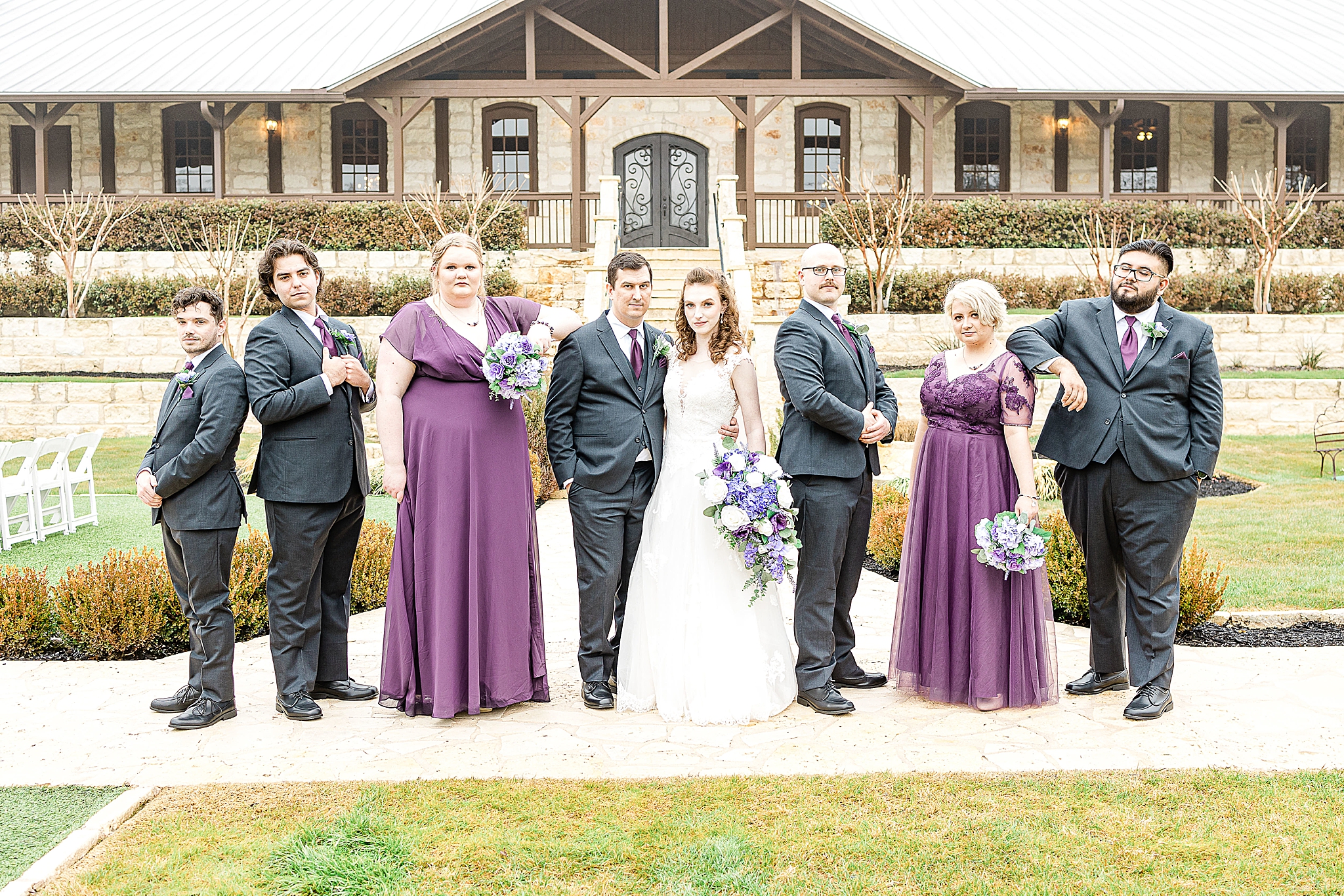 wedding party in grey and plum pose outside Stone Hall at the Springs