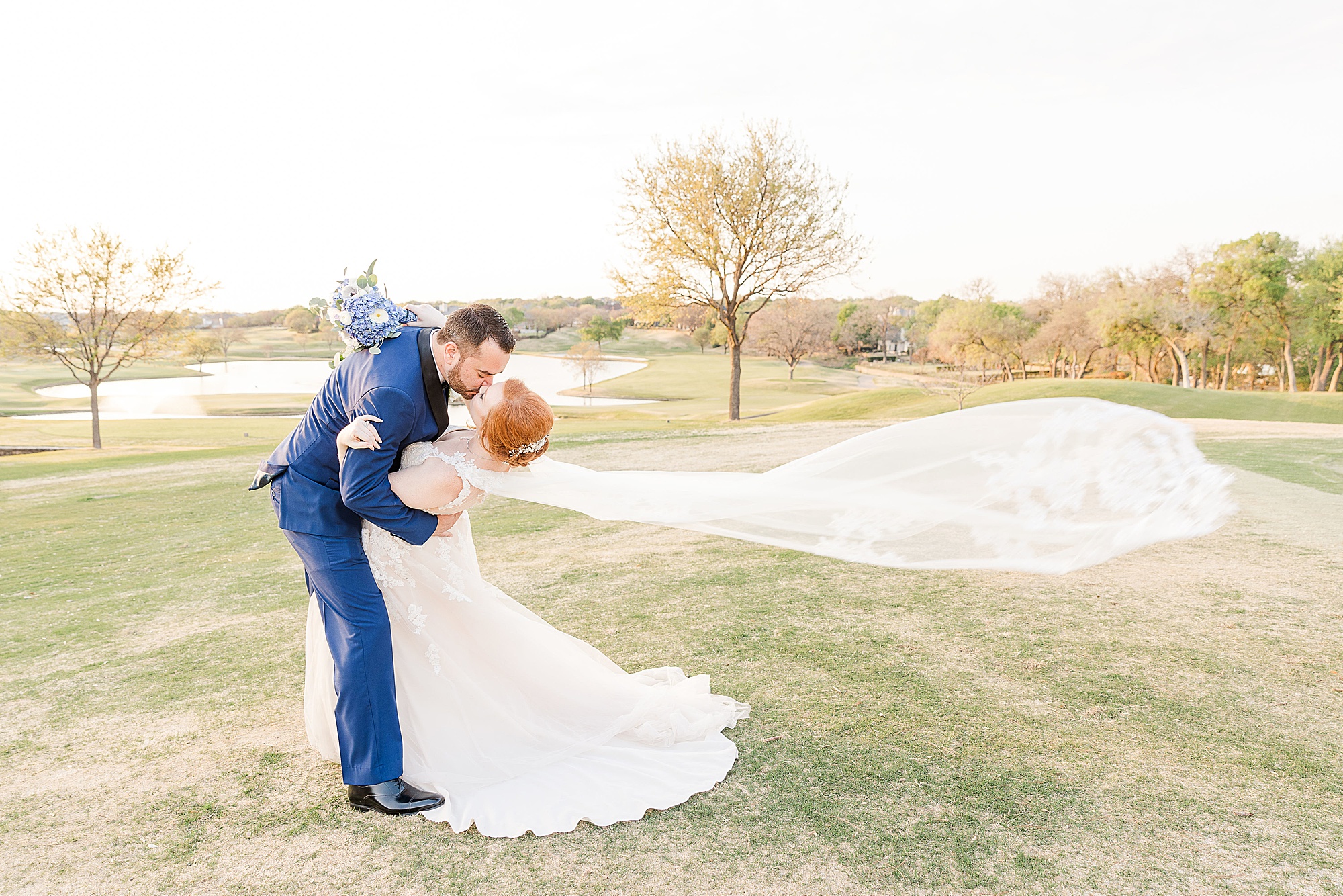 bride and groom kiss during wedding photos at Stonebriar Country Club with bride's veil floating