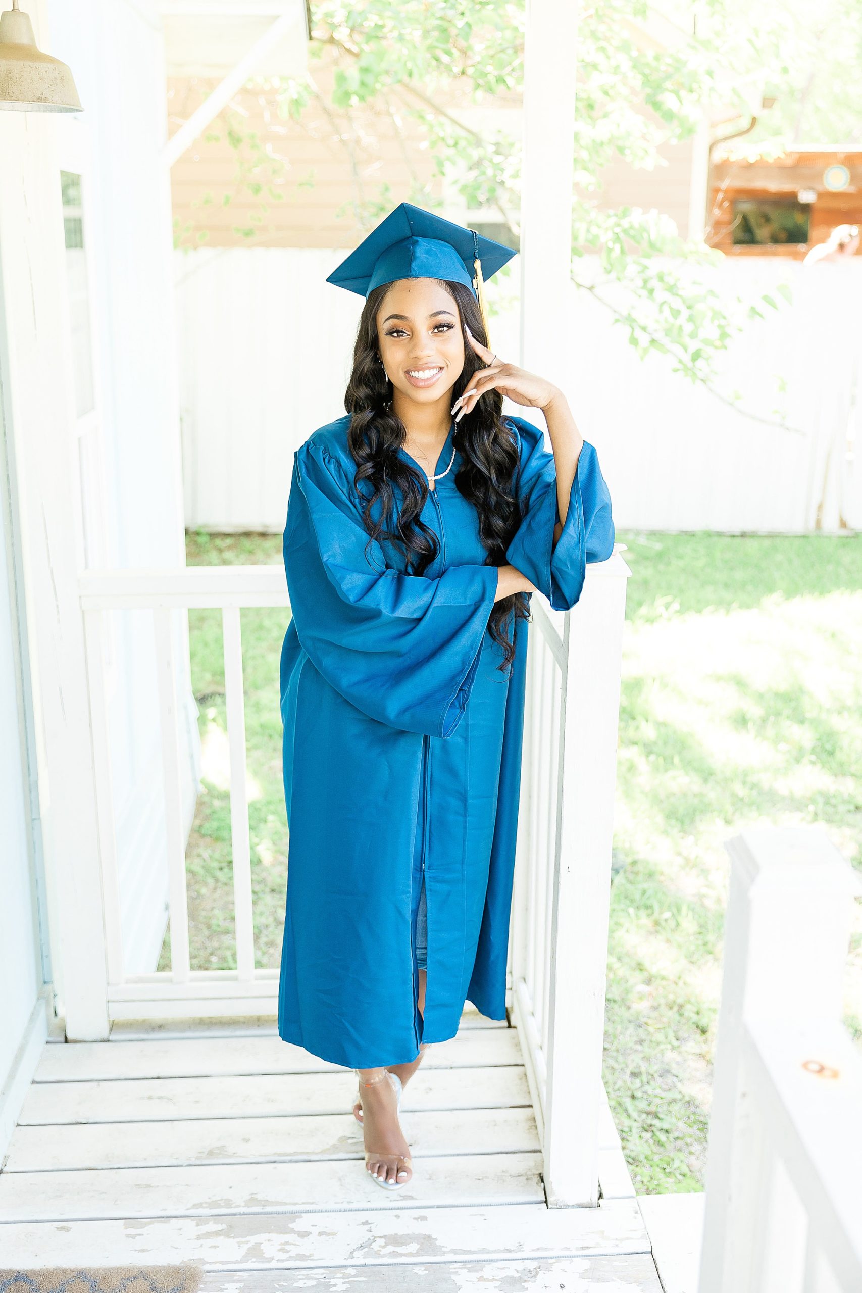 senior in cap and gown poses on front porch of Studio House