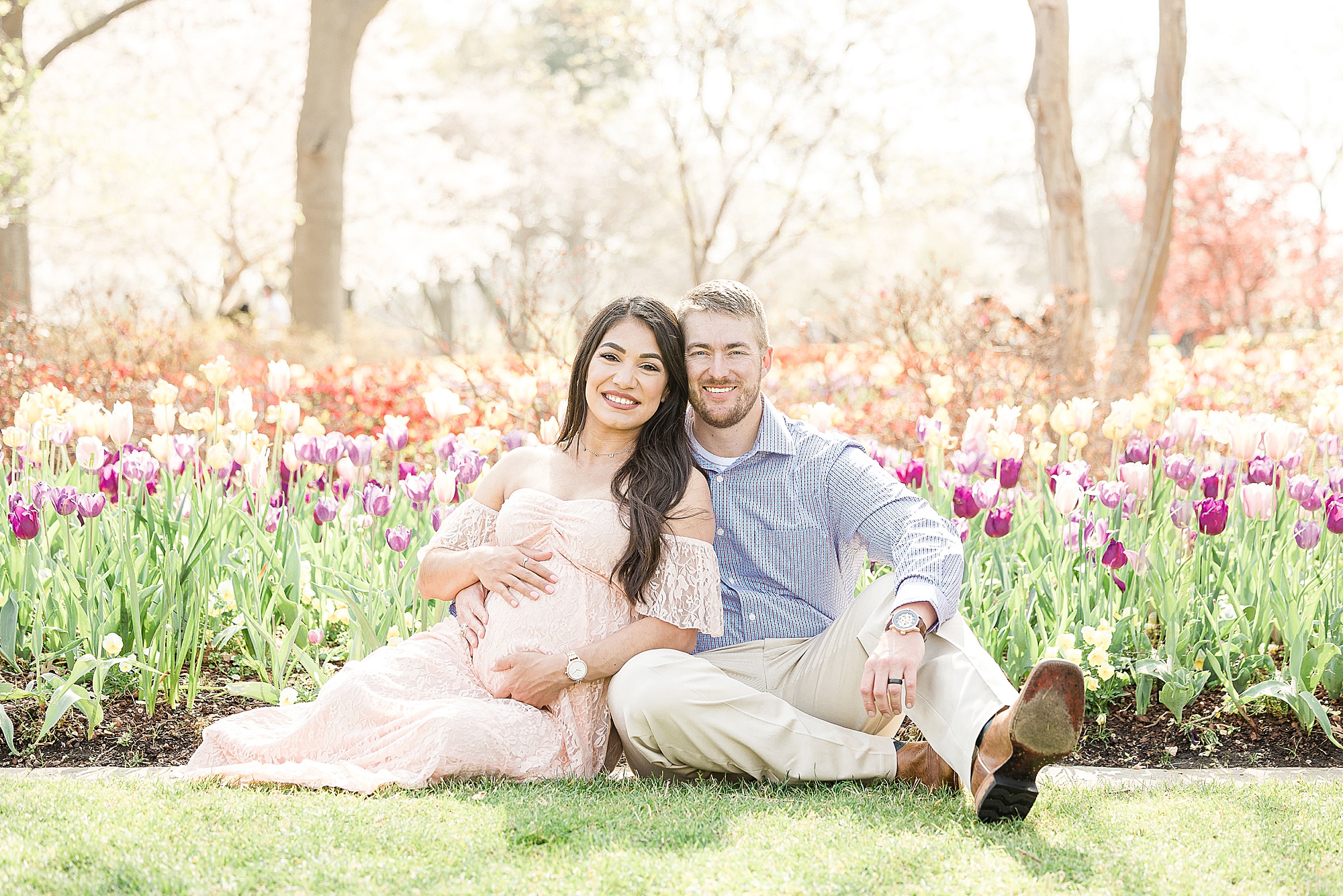 couple expecting baby sits by bed of tulips