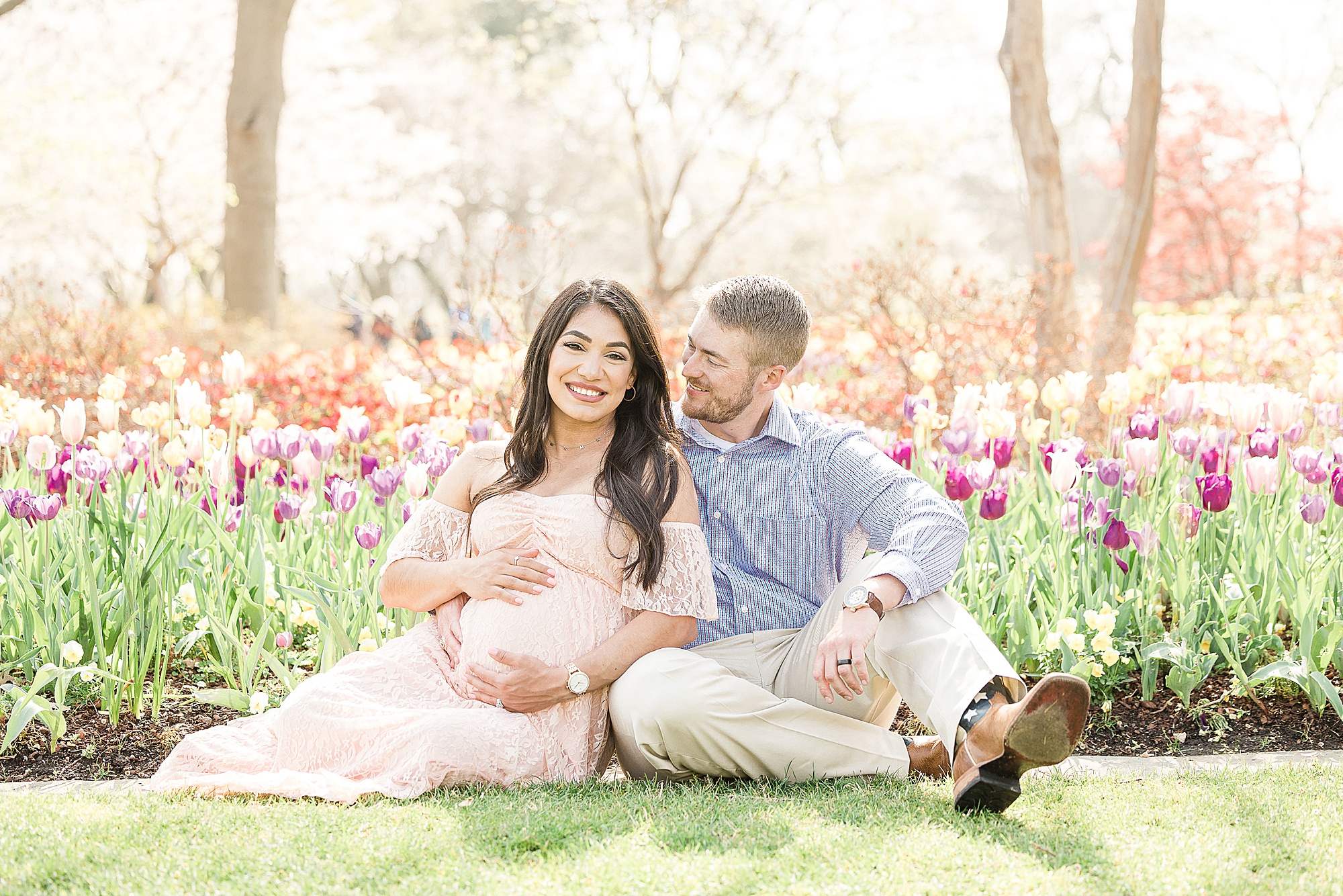 expecting parents sit in front of tulip beds at Dallas Arboretum