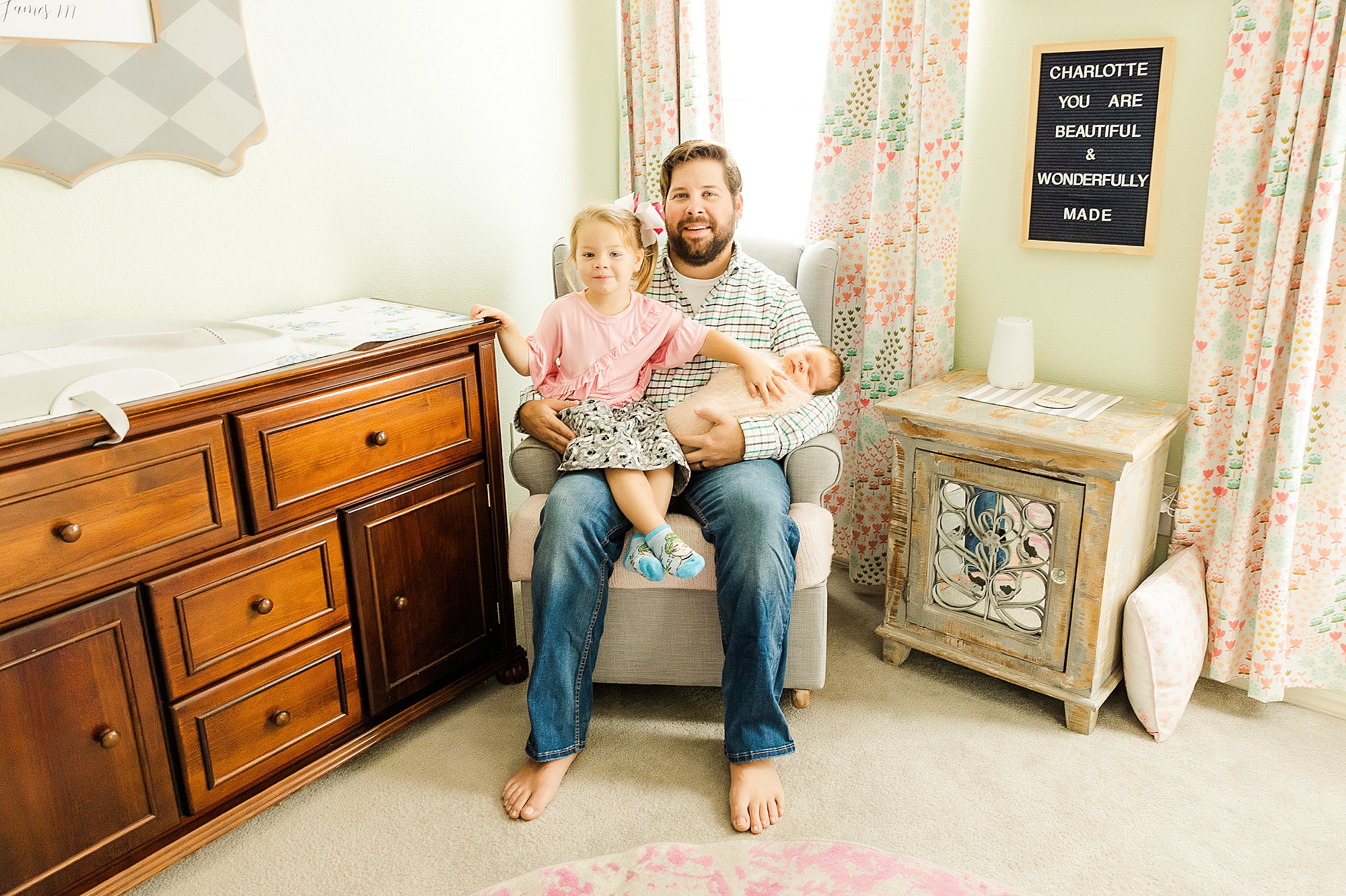 dad sits in rocking chair with daughters during Krum lifestyle newborn session