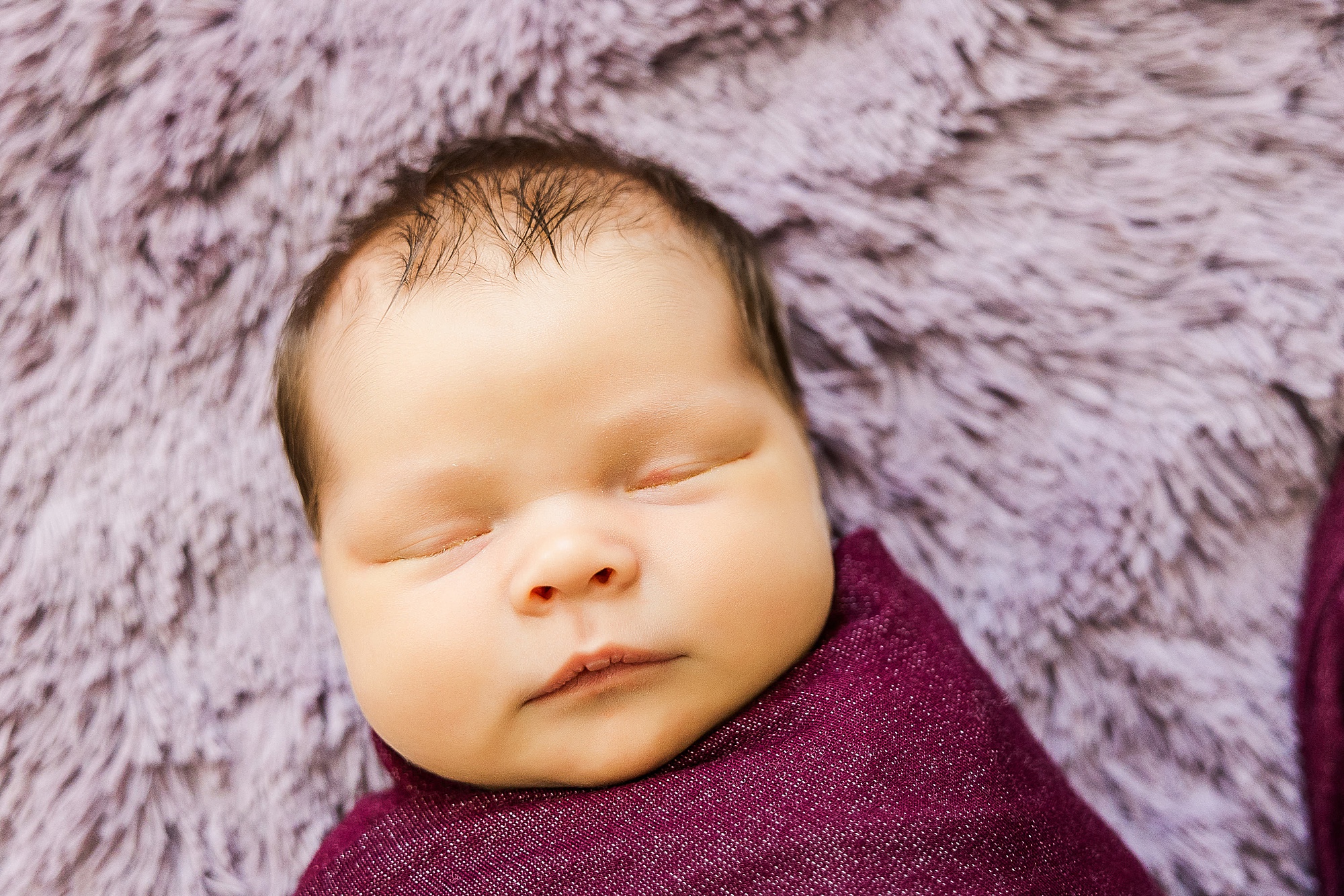 baby in purple wrap lays on purple rug during newborn photos
