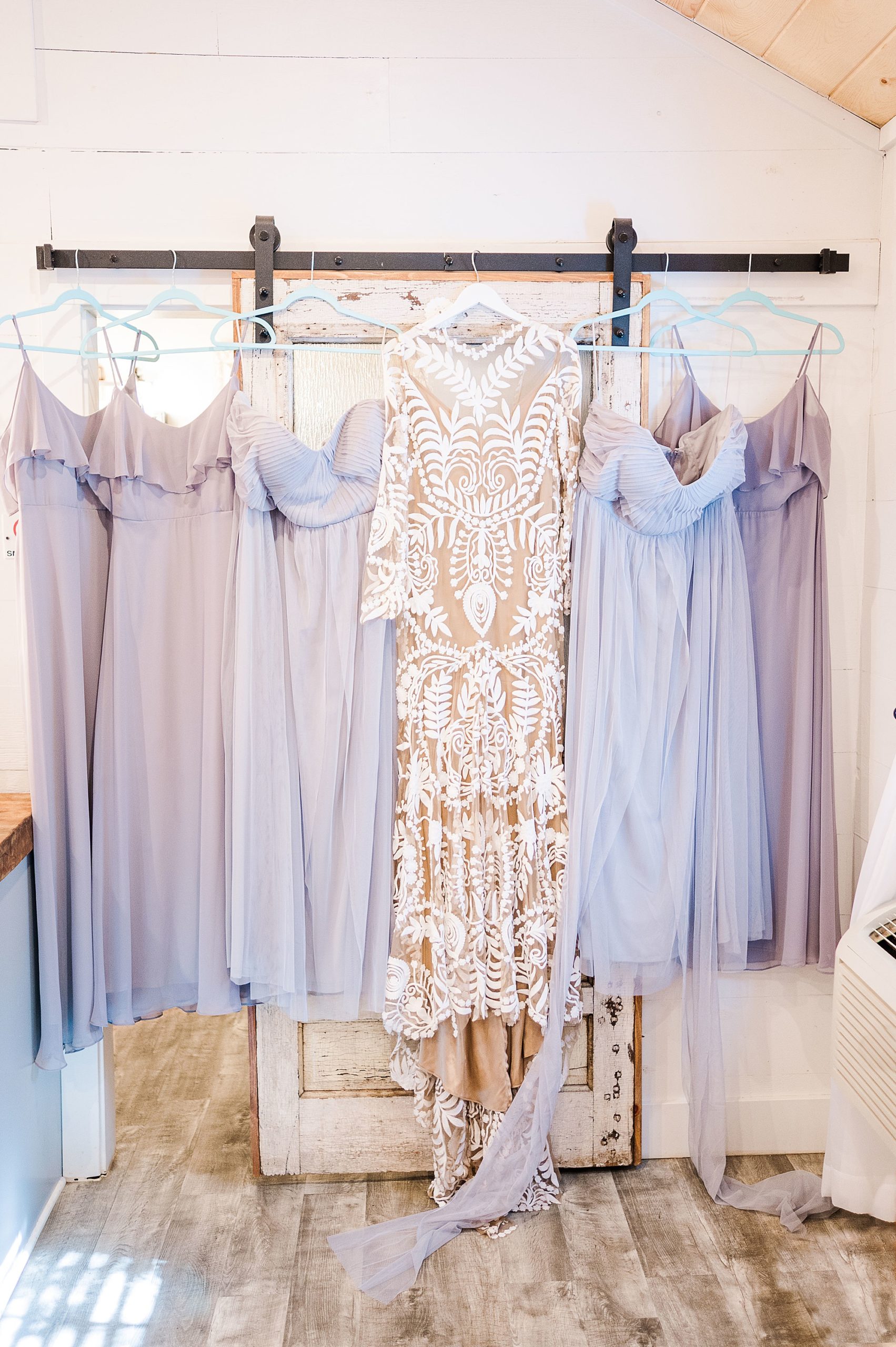 wedding dress hangs on wall with bridesmaid gowns 