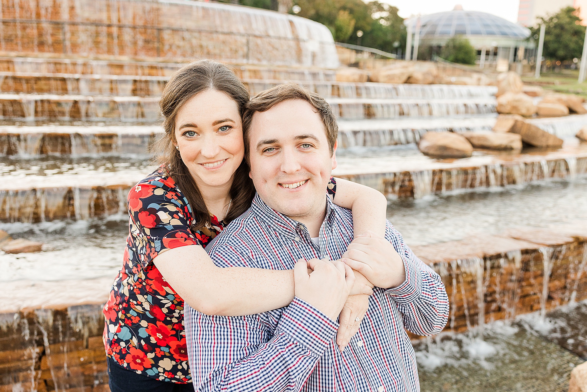 bride hugs groom from behind during Shreveport engagement session by fountain