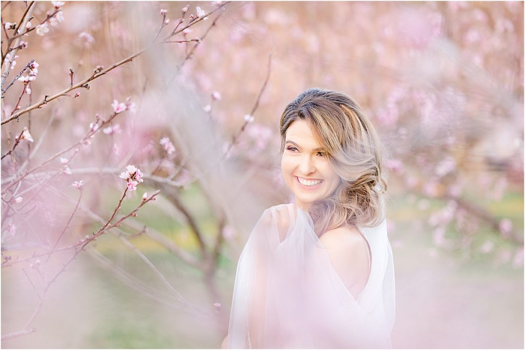 bride with sideswept bangs in peach orchard with blooming peach trees