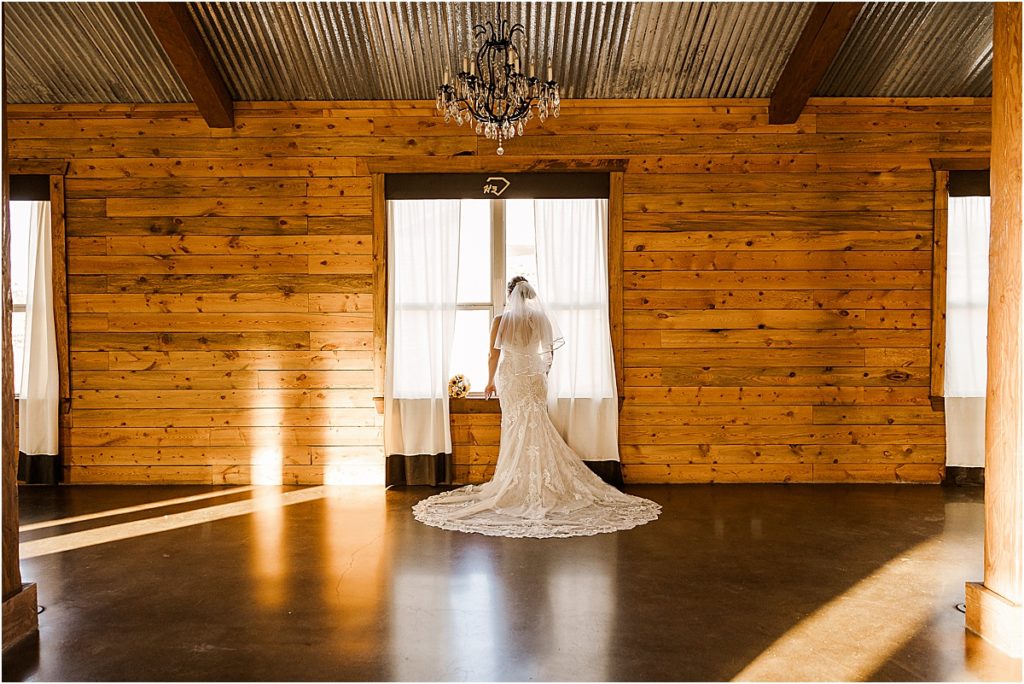 bride in white lace dress looking out of window in rustic barn wedding venue