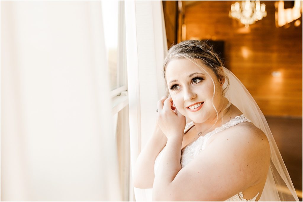 bride with veil adjusting earring looking out of window at wedding venue for stand-alone bridal session