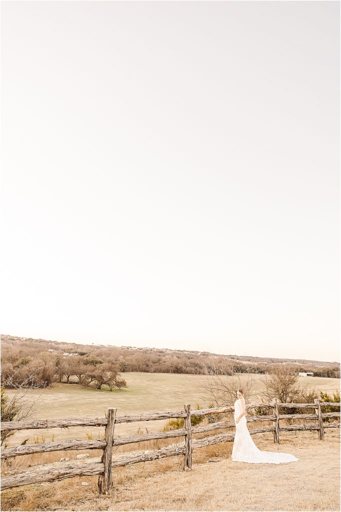 bride in white lace dress looking out over hill and field 